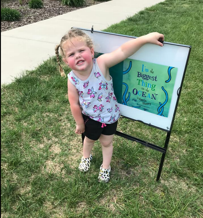 Young student in Holton next to a StoryWalk.